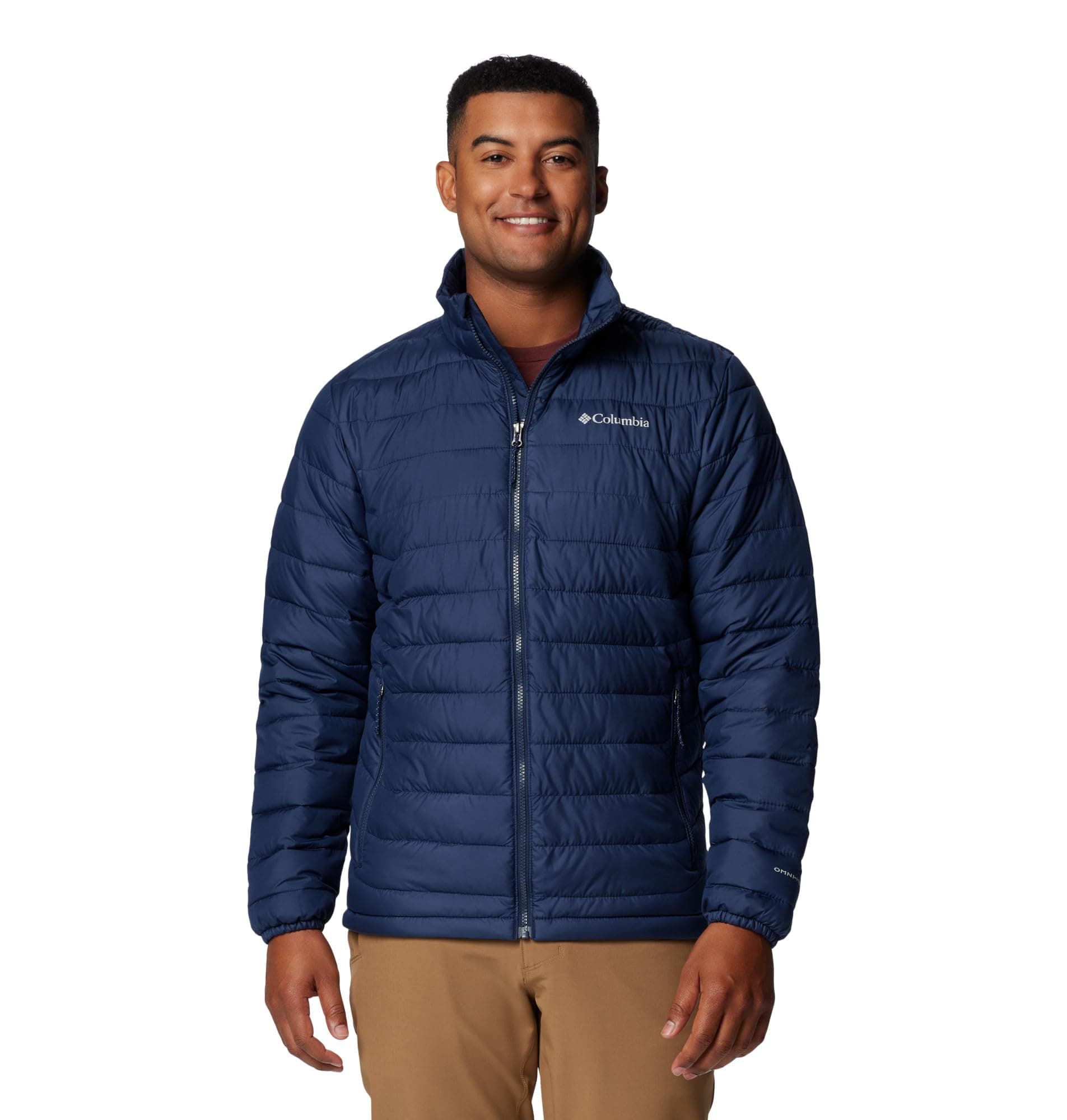 Hombre sonriendo con chaqueta acolchada azul marino Columbia Powder Lite II sobre camiseta granate y pantalones beige, listo para la nieve.